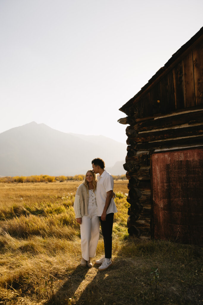 couple standing in front of barn in aspen surrounded by trees