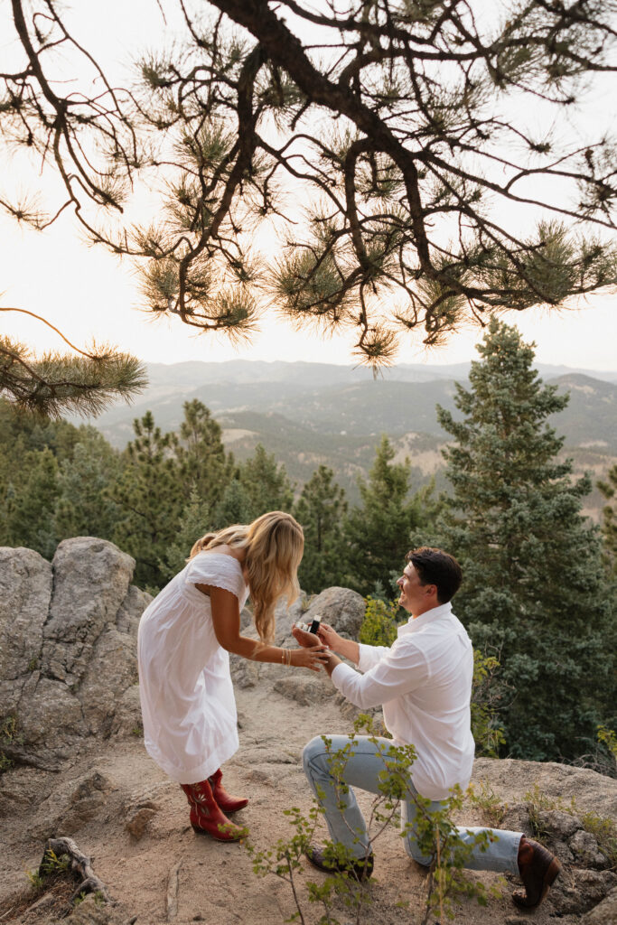 woman getting proposed to on cliffside of boulder 