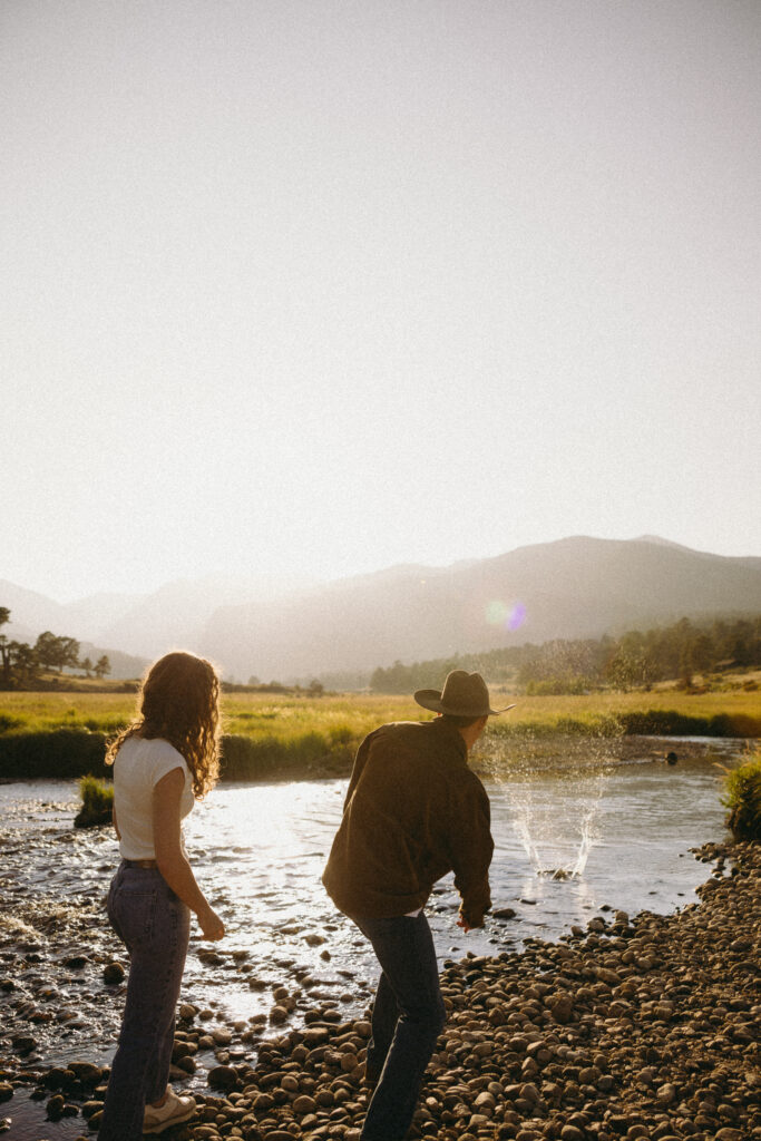 couple skipping rocks in water at rocky mountain national park during their colorado engagement