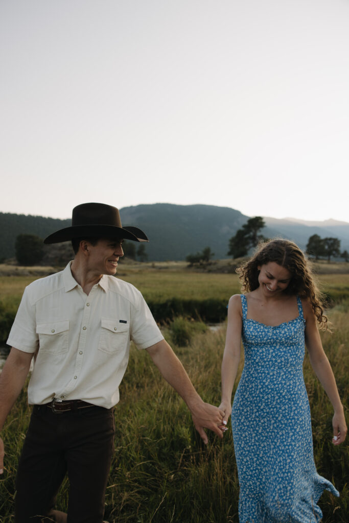 couple holding hands in open field at rocky mountain national park during their colorado engagement