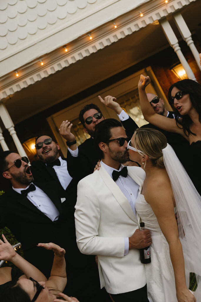 A luxe timeless wedding day in Scottsdale Arizona wedding with bride and groom kissing with their wedding party huddle around them