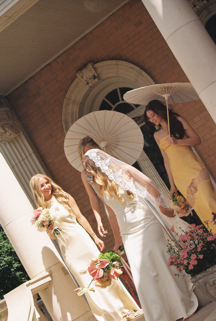 bride and bridesmaids holding parasols while walking down the steps at venue