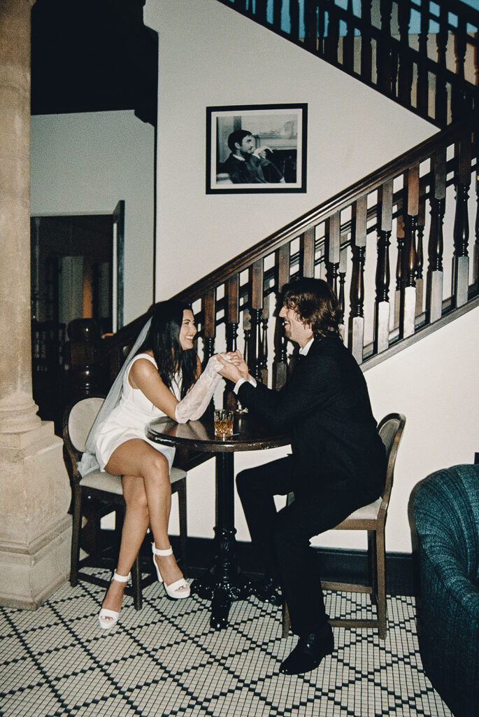 bride and groom on film sitting at a bar and holding hands