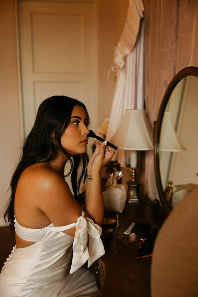 bride doing her blush in the mirror of the bridal suite of wrigley mansion before wedding