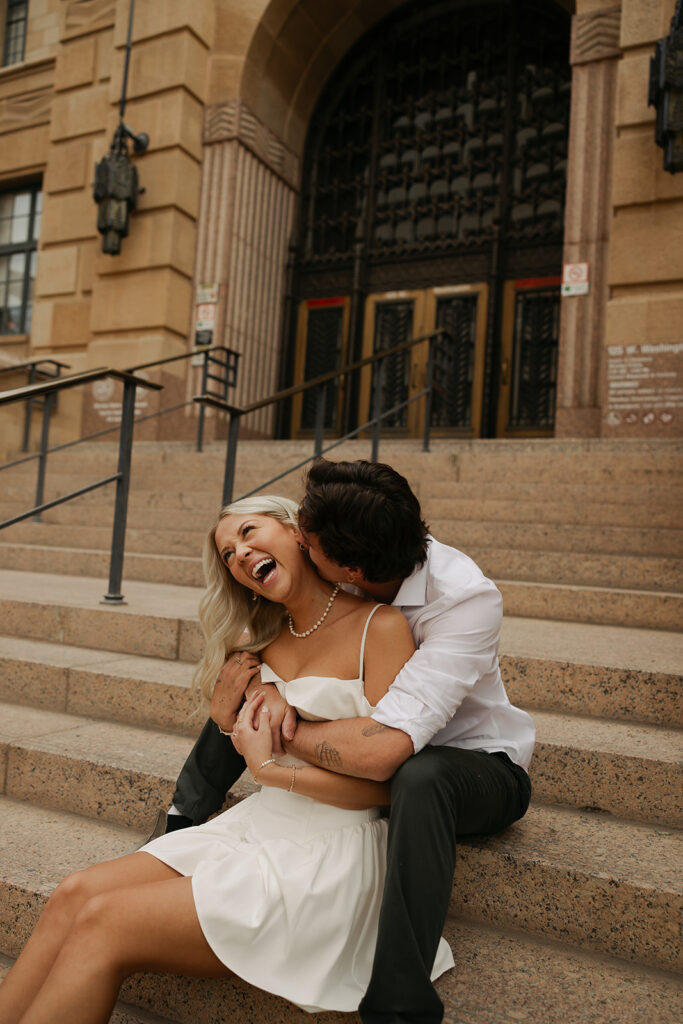 couple sitting on steps laughing during downtown phoenix engagement photos 