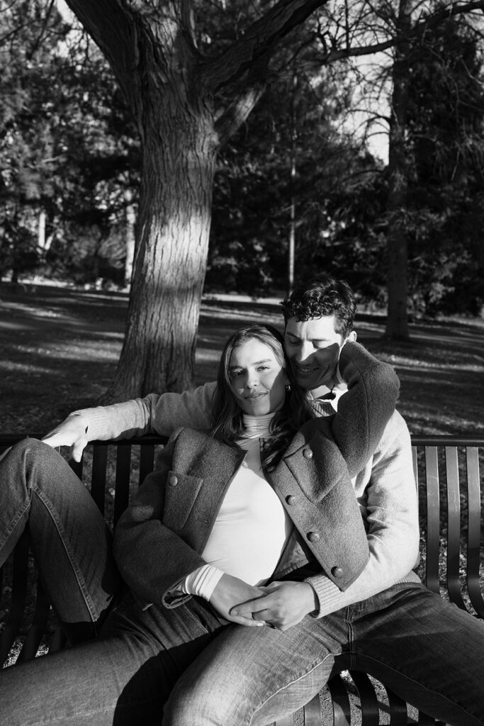 couple sitting on bench at cheesman park in denver during their colorado engagement photos