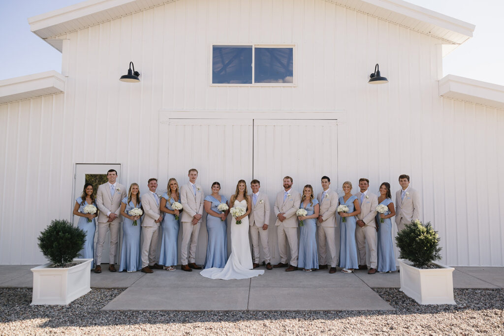 the bridal party in cream and baby blue in front of a white barn at vista view events