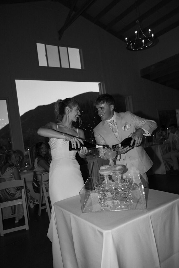 black and white of bride and groom pouring champagne into a champagne tower