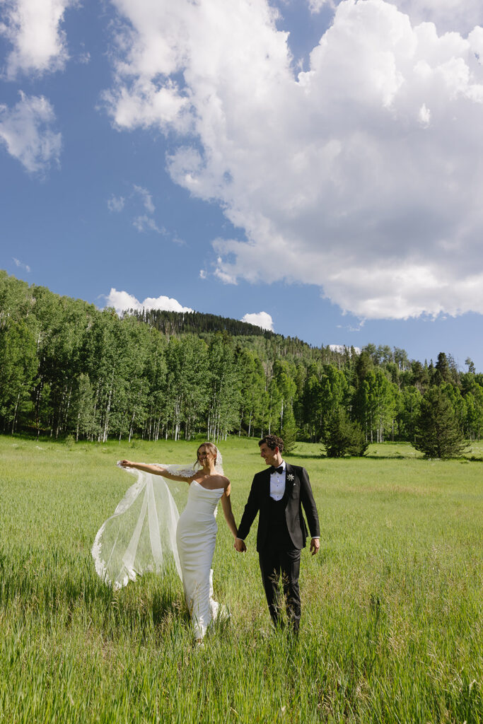 bride and groom walking in a field by the mountains