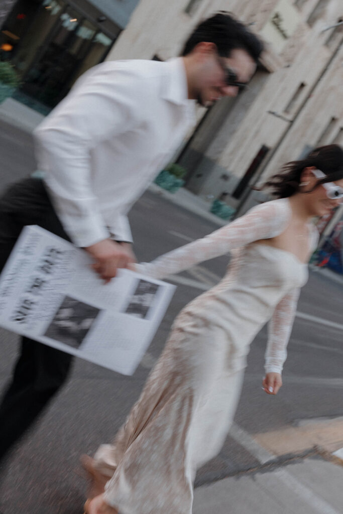 couple holding hands and running in the city with save the date newspaper