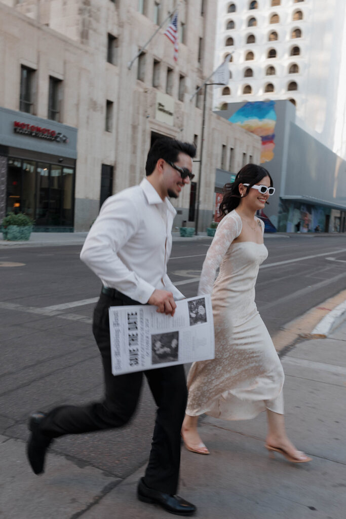 couple holding hands and running in the city with save the date newspaper