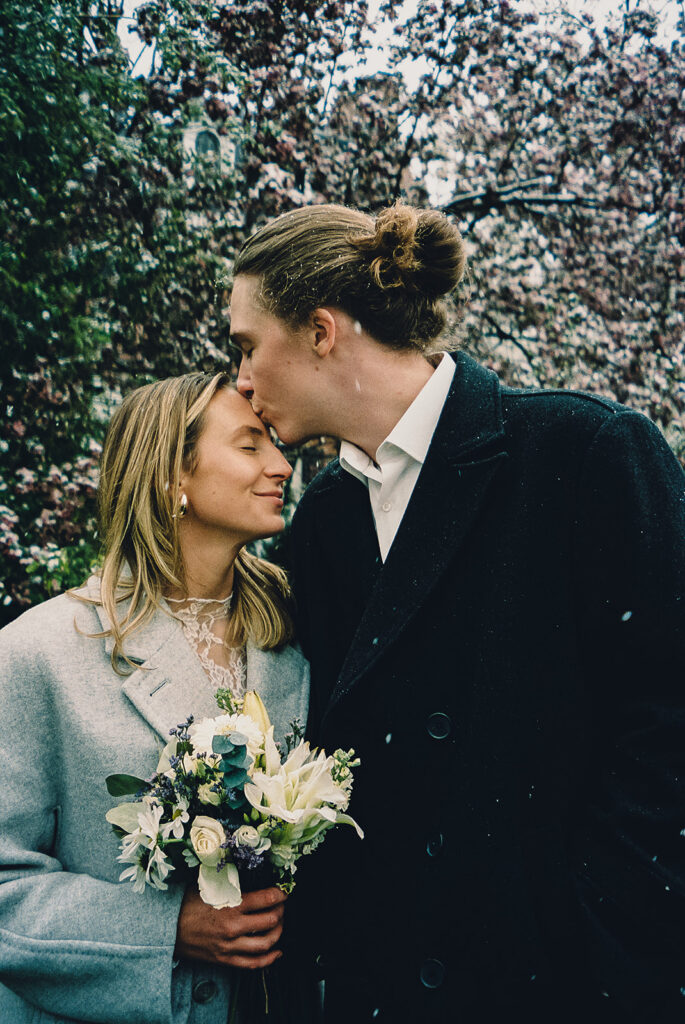 groom kissing bride on the forehead in the rain