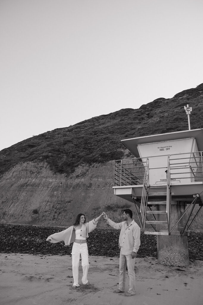 black and white photo of a couple spinning around on the beach
