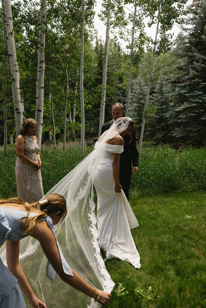 maid of honor helps bride adjust veil for first look with dad